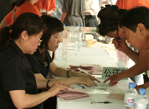 Two notary officials check the documents of voters at the venue for a vote on demolishment and reconstruction of old buildings in Juixiaqiao Sub-district in Beijing, June 9, 2007. Local government and the real estate developer jointly organize the vote on Saturday to see if majority residents of over 5000 families accept the new compensation policy after failed attempts to reach an agreement through other ways. Both notary officials and supervisors are invited to monitor the vote that runs from 9 a.m. to 9 p.m. at six ballot booths. [Sun Yuqing/m.ming7.cn]